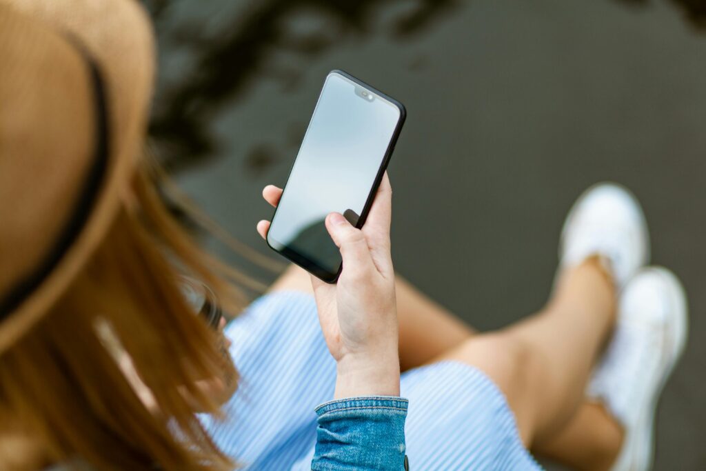 pexels-photo-1310532-1310532 A young woman holding a smartphone while sitting outdoors in summer, capturing a moment of relaxation and technology use.